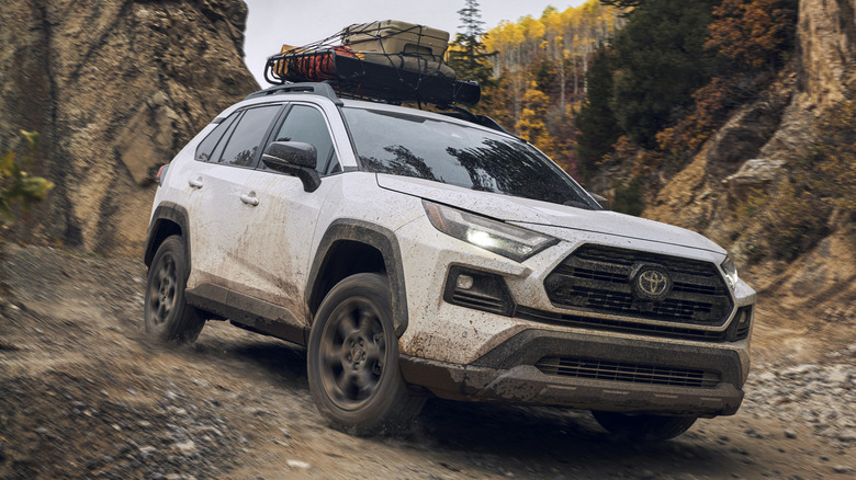 A white 2024 Toyota RAV4 Hybrid SUV on a rocky trail with a load of cargo on its roof