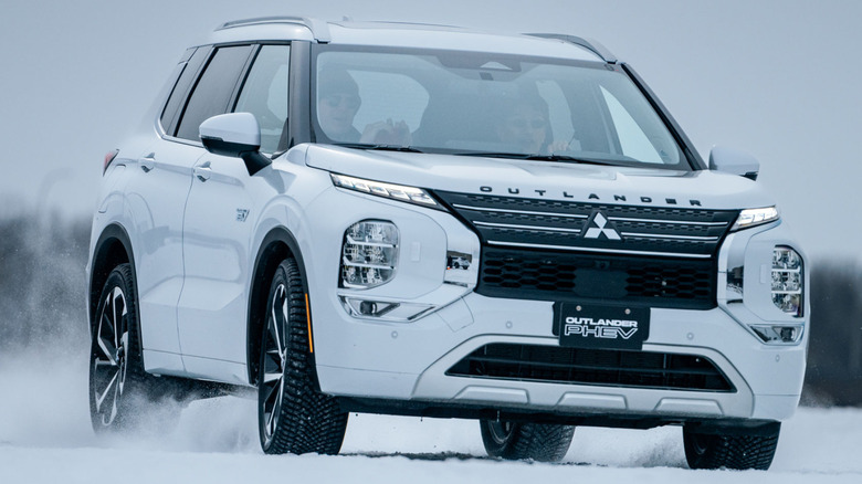 A white 2024 Mitsubishi Outlander Plug-in Hybrid SUV driving in snow