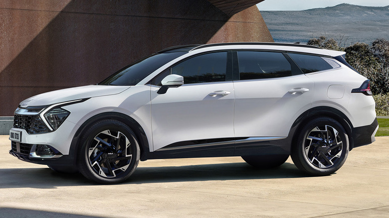 A white 2023-plus Kia Sportage SUV parked in front of an abstract concrete structure