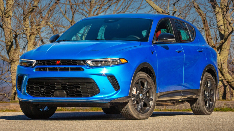 A blue 2024 Dodge Hornet R/T plug-in hybrid SUV parked in front of low leafless trees