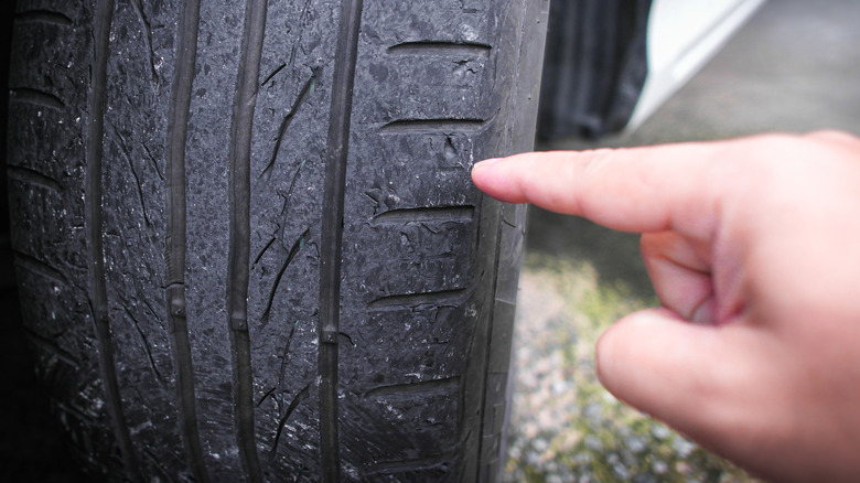 A hand pointing to a worn out tire.