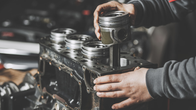 Mechanic installs pistons into an engine block's cylinders