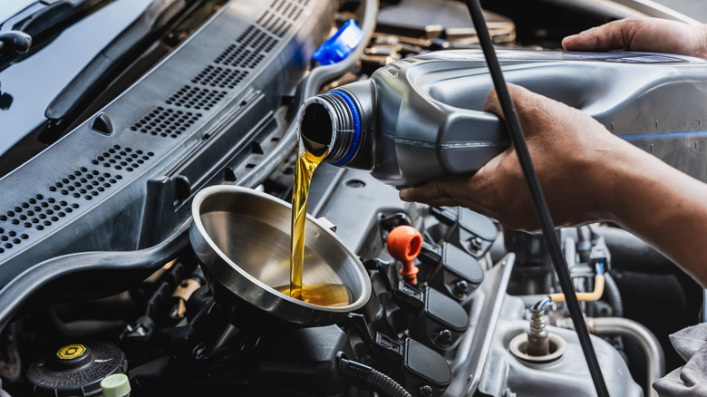 Car mechanic pouring engine oil into vehicle.