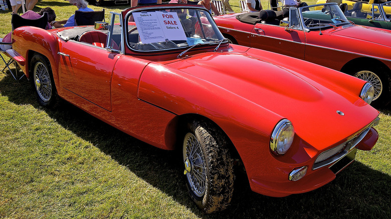 A red Reliant Sabre 4 convertible with the top down parked on the grass with a for sale sign in the windshield.