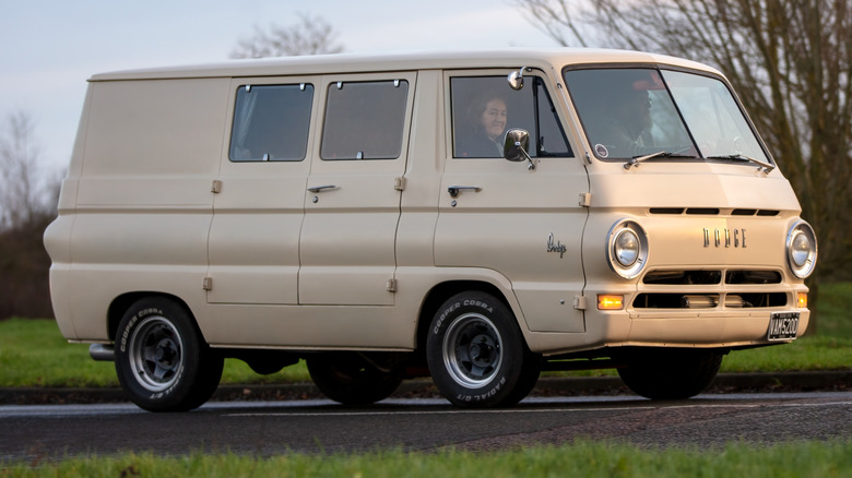 An all white Dodge A100 Van with side doors on the road.