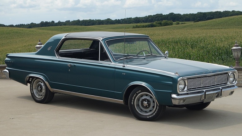 A classic blue Dodge Dart model parked outdoors near grass.