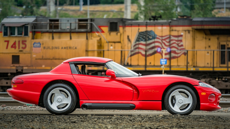 The passenger side of a red Dodge Viper with a train in the background.