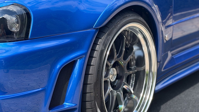 A blue car sports aftermarket rims and performance tires