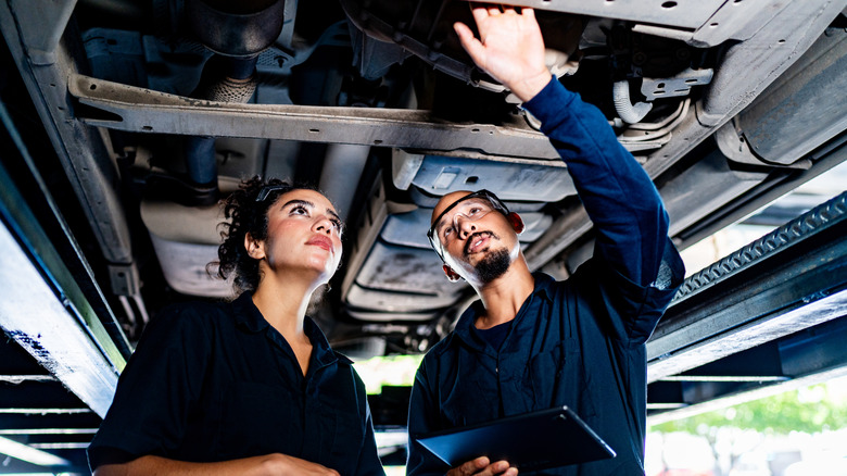 Two people looking at a vehicle while standing beneath it, as the car sits on a hydraulic lift