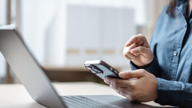 A person works on a phone and laptop.
