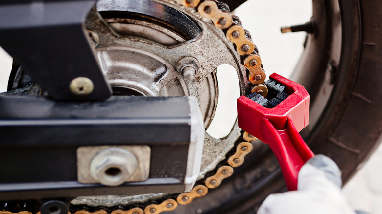 A person using a specialized brush to clean a motorcycle chain.