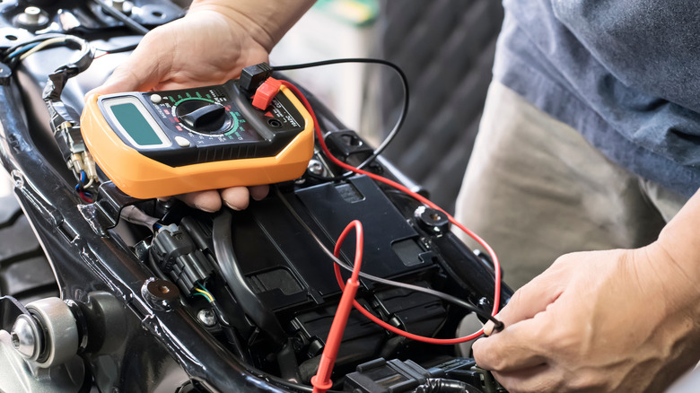 A person using a digital multimeter on a motorcycle.
