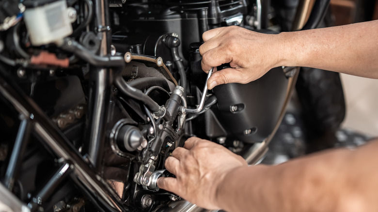 A person using a hex wrench on a motorcycle bolt.