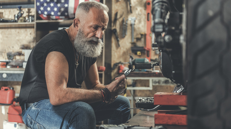 A person puzzles over tools working on a motorcycle in a home garage.