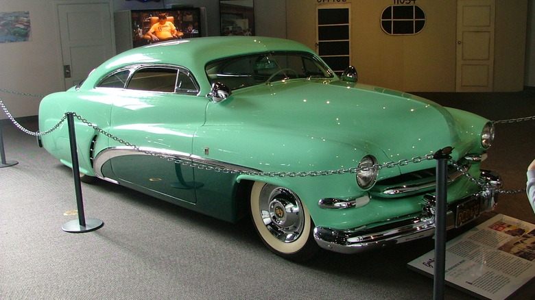 Front-three-quarter view of the 1949 Hirohata Mercury custom coupe, finished in seafoam green with a dark green side swoosh and a heavily chopped roofline on display inside a museum exhibit.