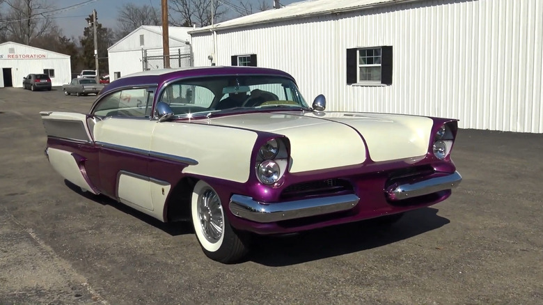 Front-three-quarter view of a custom 1957 two-tone El Capitola custom-built coupe painted in cream white and deep metallic purple, featuring custom tunneled quad headlights, low stance, and sweeping rear tailfins.
