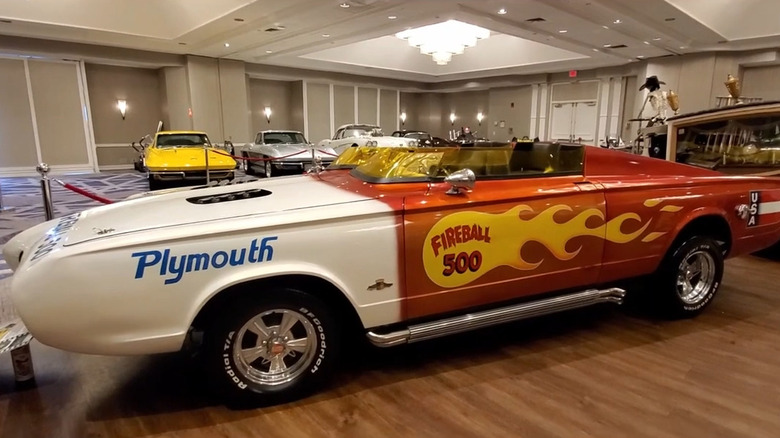 Side profile of the 1966 Fireball 500 custom roadster on display, featuring a split white and orange paint scheme with yellow flame graphics, twin yellow Plexiglas wind deflectors, and side pipes.