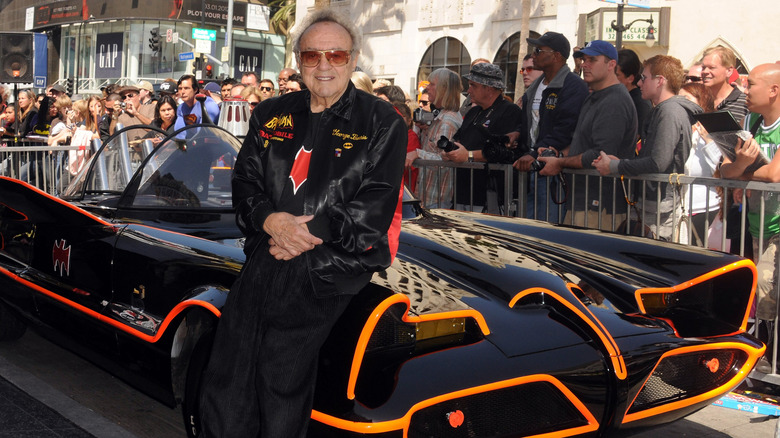 The 1966 Batmobile's front fascia, featuring glossy black paint outlined in bright fluorescent orange pinstriping around the mesh grille, a recessed headlight cavity, and creator George Barris.