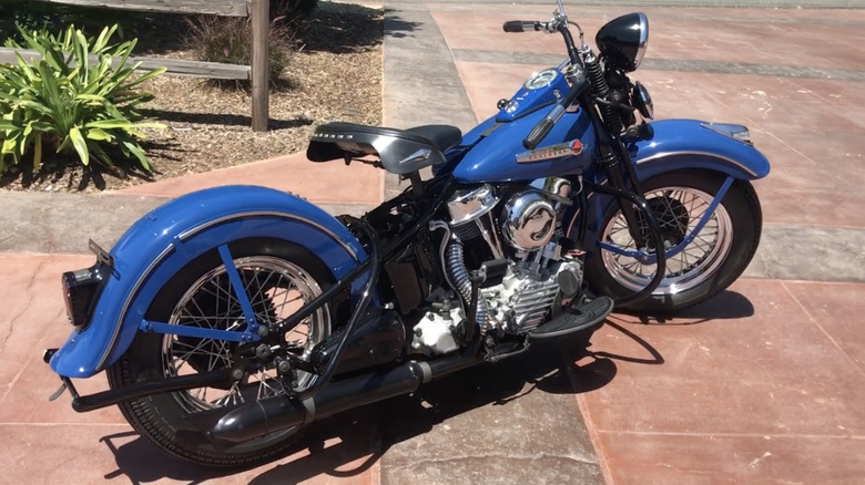 A blue 1948 Harley-Davidson FL Panhead with black and chrome accents on a paved sidewalk.