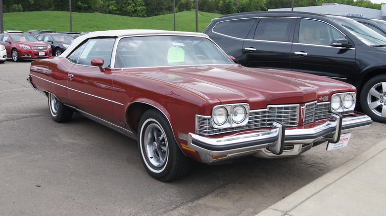 Red 1973 Pontiac Grand Ville convertible seen from front right in a dealership parking lot