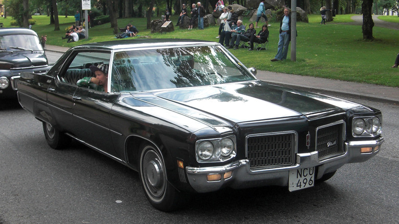 Black 1971 Oldsmobile Ninety-Eight sedan seen from right front in a vintage car parade