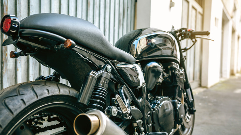 The rear of a motorcycle is photographed against a building with an emphasis on the seat.