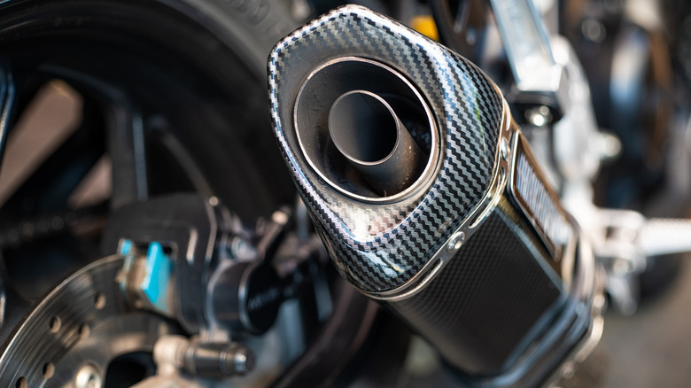 A motorcycle tailpipe with sooty deposits is photographed up close.