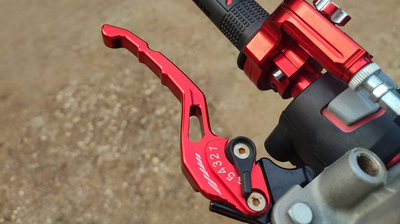 A red motorcycle hand control is photographed up close, showing adjustability.