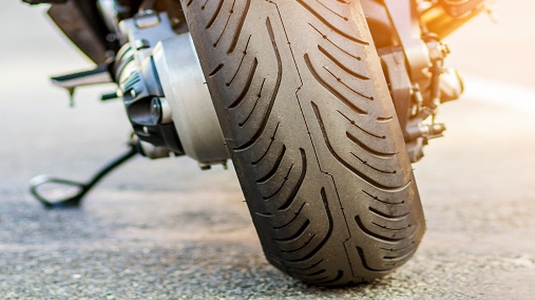 The tire of a motorcycle is viewed up close with sunlight coming from above.