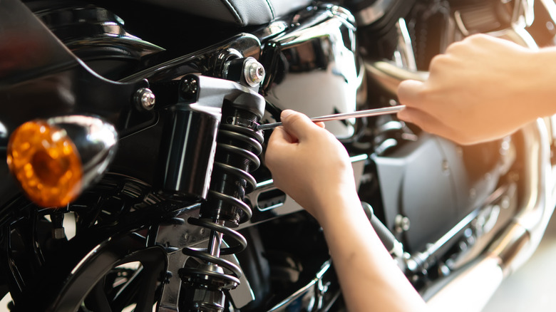 Hands adjust a motorcycle suspension.