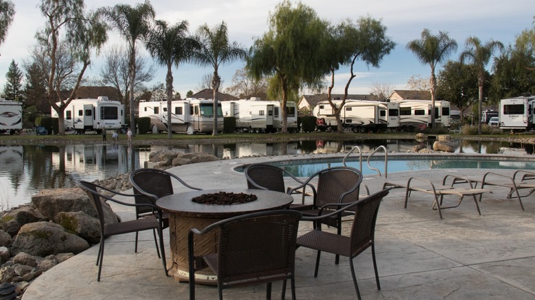 An image of a table with a firepit on a patio at an RV resort, in front of a small pool with RVs in the background