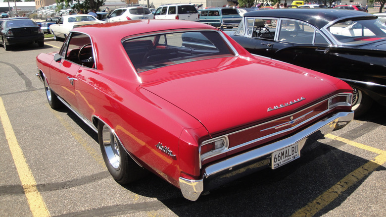 Red 1966 Chevrolet Chevelle Malibu coupe left rear three quarter view parked at outdoor car show
