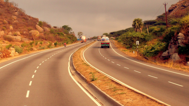 a curved section of Golden Quadrilateral highway between Bangalore and Chennai, with three trucks and a motorcycle driving through in distance