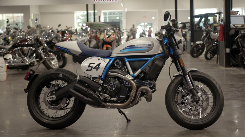 A black, silver, and blue 2020 Ducati Scrambler Cafe Racer showing the number 54 in a Ducati showroom.