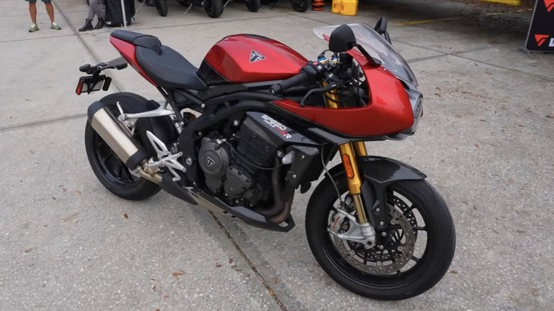 A red and black 2024 Triumph Speed Triple 1200 RR parked at a motorcycle rally on an overcast day.