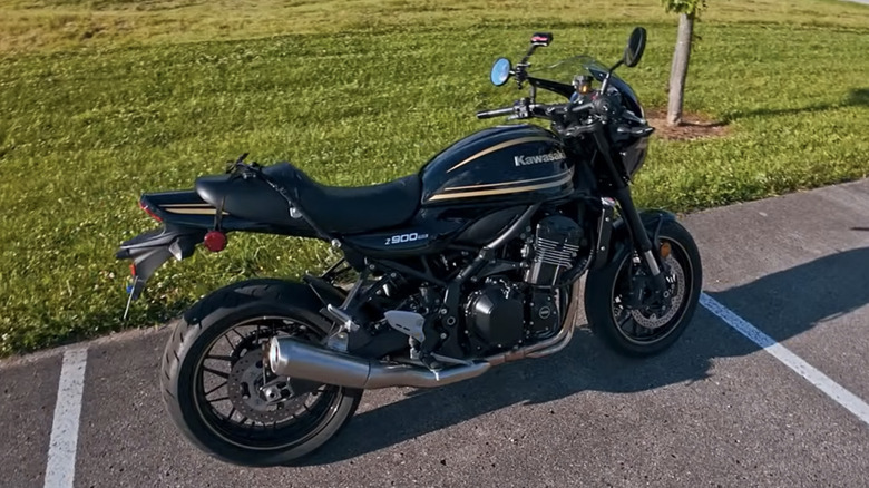 A 2025 Kawasaki Z900RS Cafe parked on a sunny day in a parking lot beside a neatly trimmed yard.