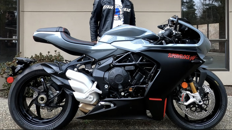 A 2025 MV Agusta Superveloce 800 parked outside a business on a cloudy day with its rider standing beside it.