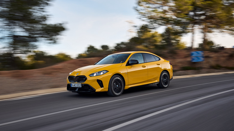 A yellow BMW 2-Series drives on a road as the landscape blurs.