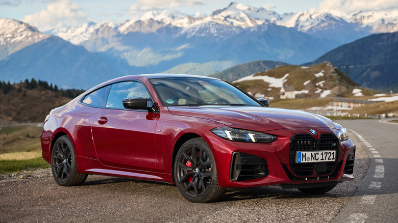 A red BMW 4 Series is parked on a road against a mountainous backdrop.