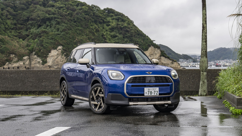 A blue Mini Countryman sits parked on a damp street.