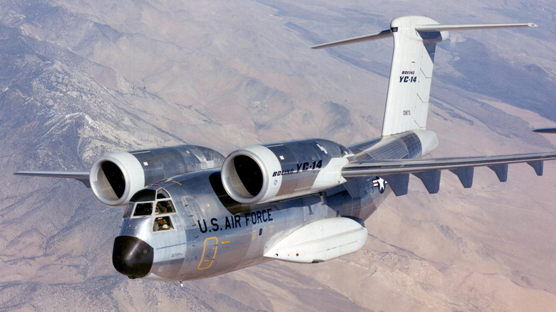 Boeing YC-14 cargo jet prototype seen from front left in flight above a desert