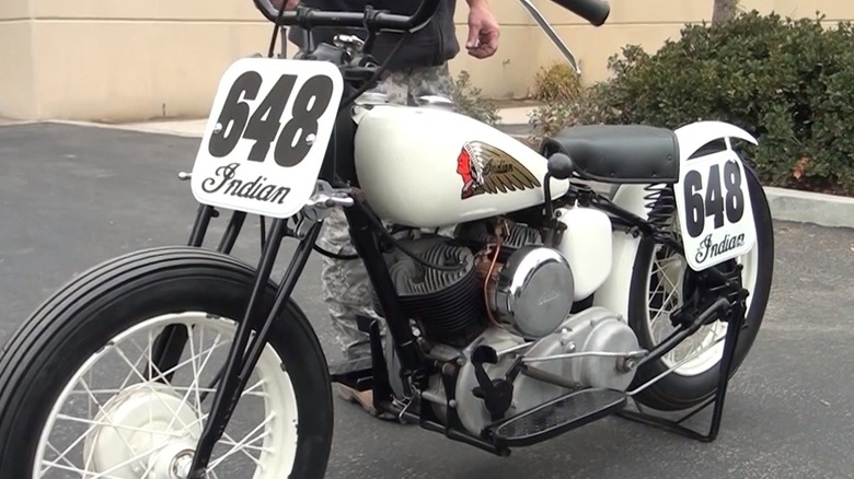 A white 1948 Indian 648 big base race bike on display in a parking lot.