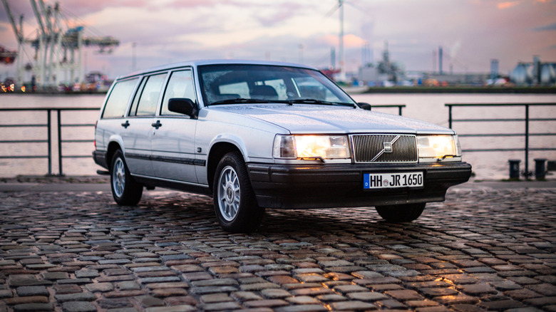 A Volvo 940 sitting on stones near a harbor.