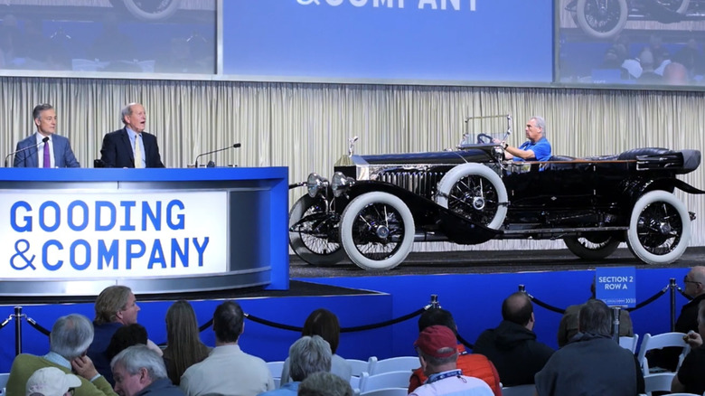 A black Rolls-Royce 40/50 HP Silver Ghost Torpédo gleams on an auction stage with a driver behind the wheel.
