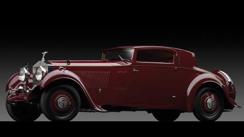 A burgundy Rolls-Royce Phantom sits dramatically in a studio against a dark background.