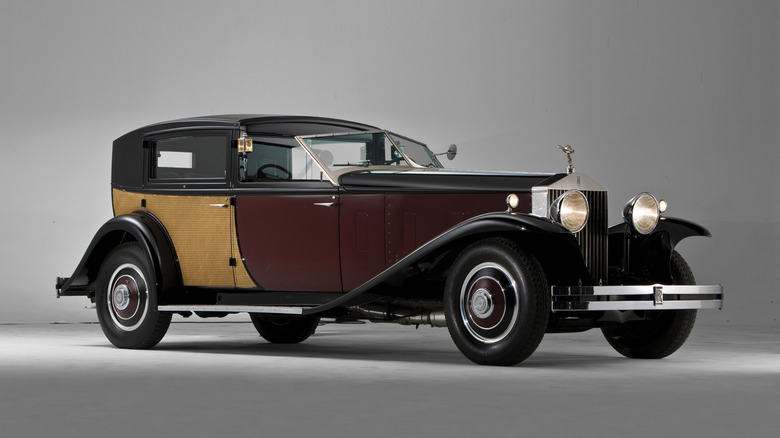 A hard-top Rolls-Royce sits in a studio with headlights lit.