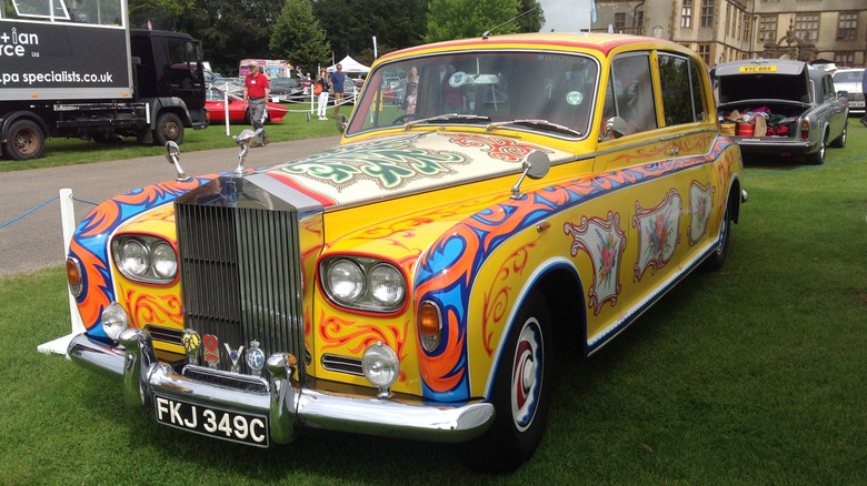 A replica of John Lennon's wildly colorful Rolls-Royce Phantom V sits on grass at a car event.