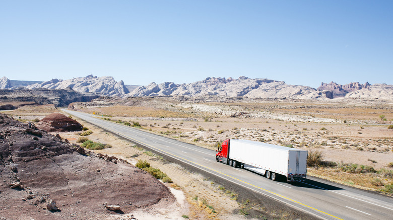 A truck driving on highway in a deserted area, mountains in the background.