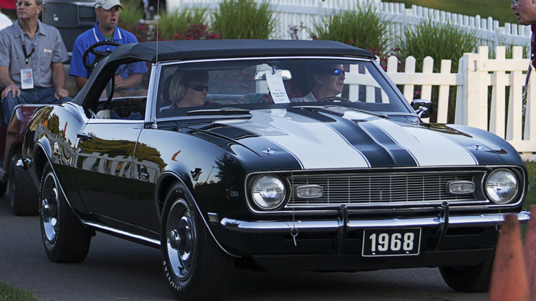The Fathom Green 1968 Chevrolet Camaro Z/28 convertible with twin white racing stripes driving in an outdoor collector car event