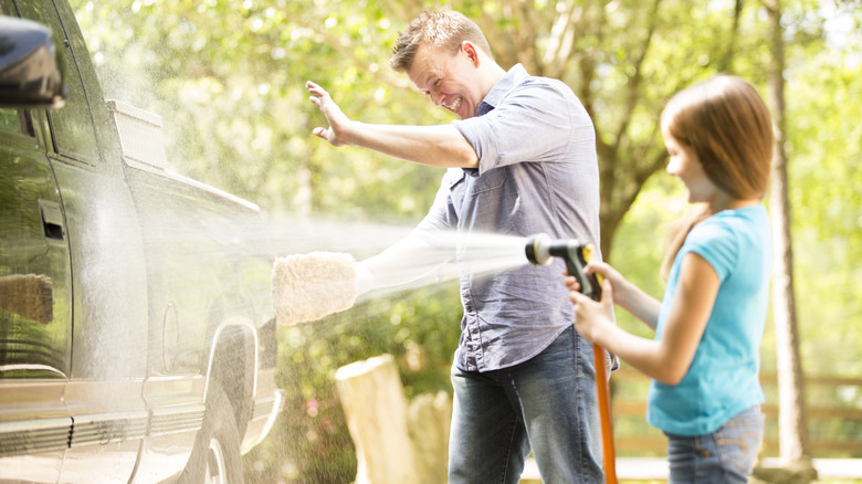 A child helps a man clean a truck by spraying a hose.